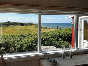 Ein Zimmer mit großem Fenster mit Blick auf eine grüne Wiese und das Meer.