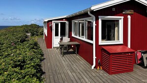 Et rødt træhus med en terrasse, et bord og en stol.