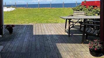 En træterrasse med havudsigt, en rød bygning og en græsplæne.