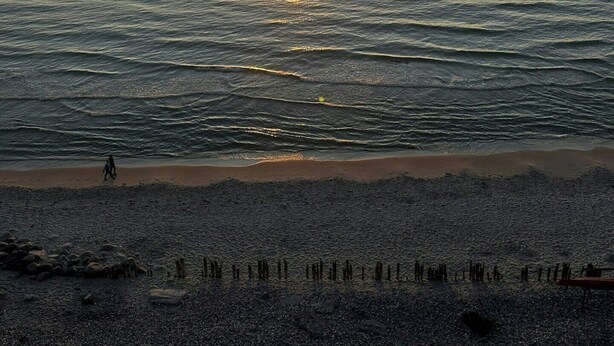 A sunset over a beach with calm water, a person walking, and scattered rocks. - Wooden house with panoramic view over Kattegat (Hundested)