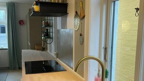 Cozinha moderna com pia de aço inoxidável, bancada de madeira e janela com vista para uma parede de tijolos.