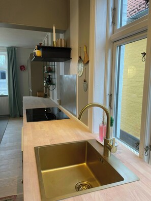 Eine moderne Küche mit einer Edelstahl-Spüle, einer Holz Arbeitsplatte und einem Fenster mit Blick auf eine Ziegelwand.