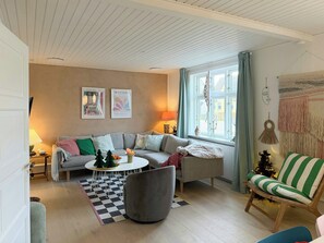 Ein Wohnzimmer mit Sofa, Sessel, rundem Couchtisch und einem kleinen Weihnachtsbaum.