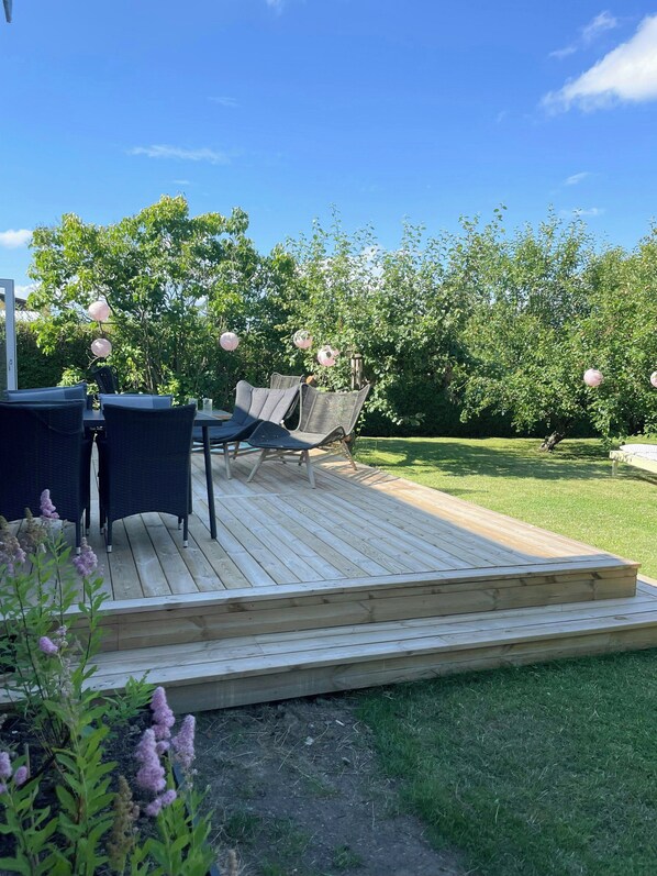 Eine Holzterrasse mit Gartenmöbeln, ein Rasen und Bäume im Hintergrund.