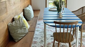 Quarto com parede de madeira, mesa listrada, tapete tecido e janela com vista para vegetação.
