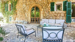 A stone building with a stone archway, green shutters, a white sofa, and a table with chairs. - 1700s design stone house in Mallorca with pool (Soller)
