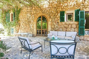A stone building with a stone archway, green shutters, a white sofa, and a table with chairs. - 1700s design stone house in Mallorca with pool (Soller)