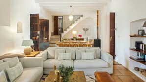 A living room with a sofa, coffee table, lamp, and a staircase leading to a dining area. - 1700s design stone house in Mallorca with pool (Soller)