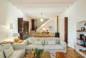 A living room with a sofa, coffee table, lamp, and a staircase leading to a dining area. - 1700s design stone house in Mallorca with pool (Soller)