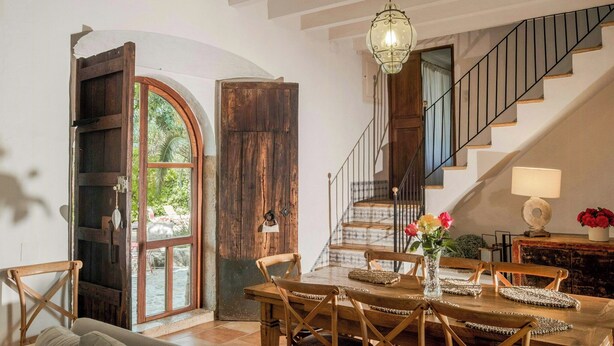 A dining area with a wooden table and chairs, a hanging light fixture, and a staircase with a railing. - 1700s design stone house in Mallorca with pool (Soller)