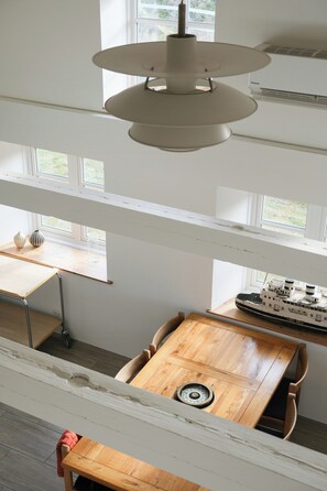 Ein Zimmer mit hohen Decken, einem Holztisch, einer Hängeleuchte und einem Schiffmodell auf einem Regal.