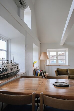 Ein Essbereich mit Holztisch und Stühlen, einem Schiffsmodell an der Wand, einer Lampe und einem Fenster mit Blick auf einen Holzzaun.