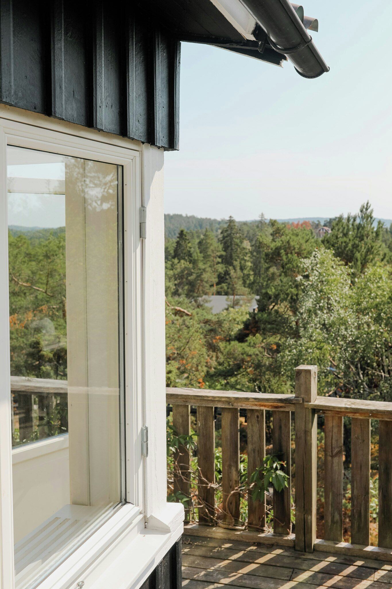 Un balcon doté d’une balustrade en bois, d’un cadre de fenêtre blanc et offrant une vue sur un paysage boisé.
