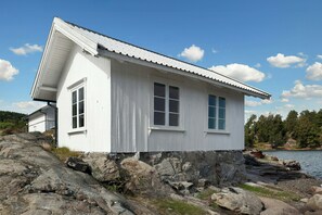 Eine weiße Holzhütte mit Satteldach, gelegen auf felsigem Gelände in der Nähe eines Gewässers.