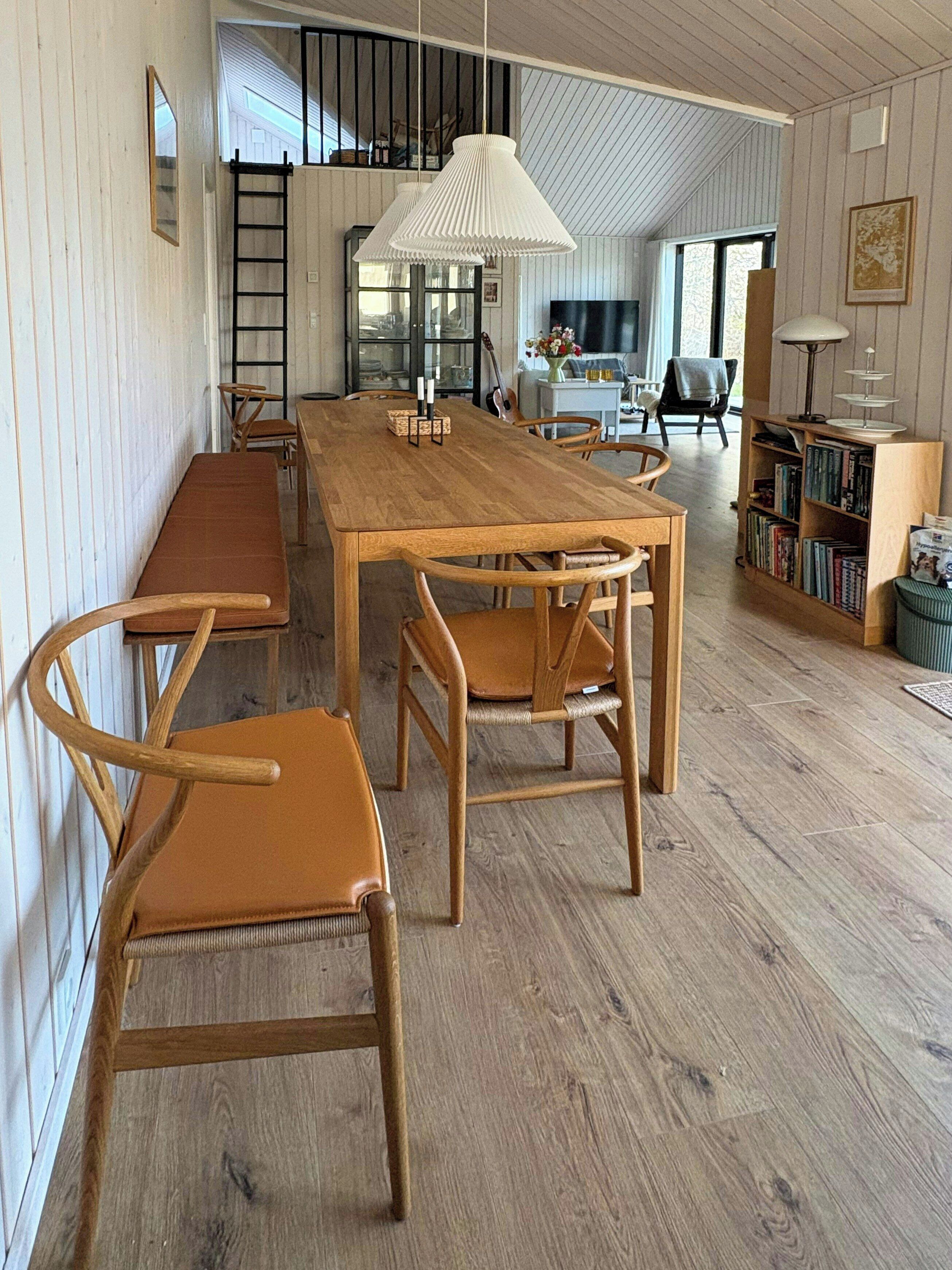 Un comedor con una mesa y sillas de madera, una estantería y una escalera apoyada en la pared.