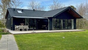 Ein modernes Haus mit großer Glasfassade, einer überdachten Terrasse und einem gepflegten Rasen.