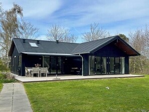 Ein modernes Haus mit großer Glasfassade, einer überdachten Terrasse und einem gepflegten Rasen.