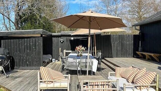 A wooden deck with a dining table, chairs, and an umbrella. - Cozy new vacation home near the water (Tisvilde)