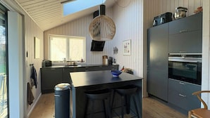 Eine moderne Küche mit einer zentralen Kochinsel, Barhocker, einem eingebauten Backofen und einem großen Fenster.