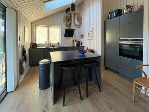 Eine moderne Küche mit einer zentralen Kochinsel, Barhocker, einem eingebauten Backofen und einem großen Fenster.