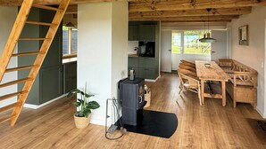 Un intérieur en bois comprenant un coin repas, une cuisine et un espace en mezzanine accessible par une échelle en bois.