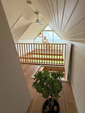 Ein Balkon mit Topfpflanze, Holzgeländer und Blick auf den Strand.