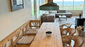 Une table à manger en bois, des bancs rembourrés, un canapé, des chaises en osier et une vue sur la mer.
