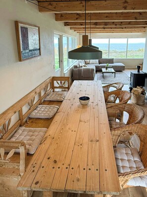 Ein Holzespeisezimmer mit gepolsterten Bänken, einer Couch, Korbstühlen und Meerblick.