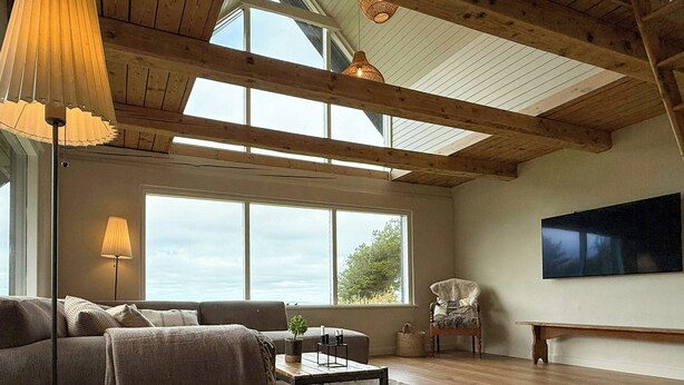 Un salon spacieux avec un plafond haut, de grandes fenêtres, un canapé, une table basse, une lampe et un fauteuil.