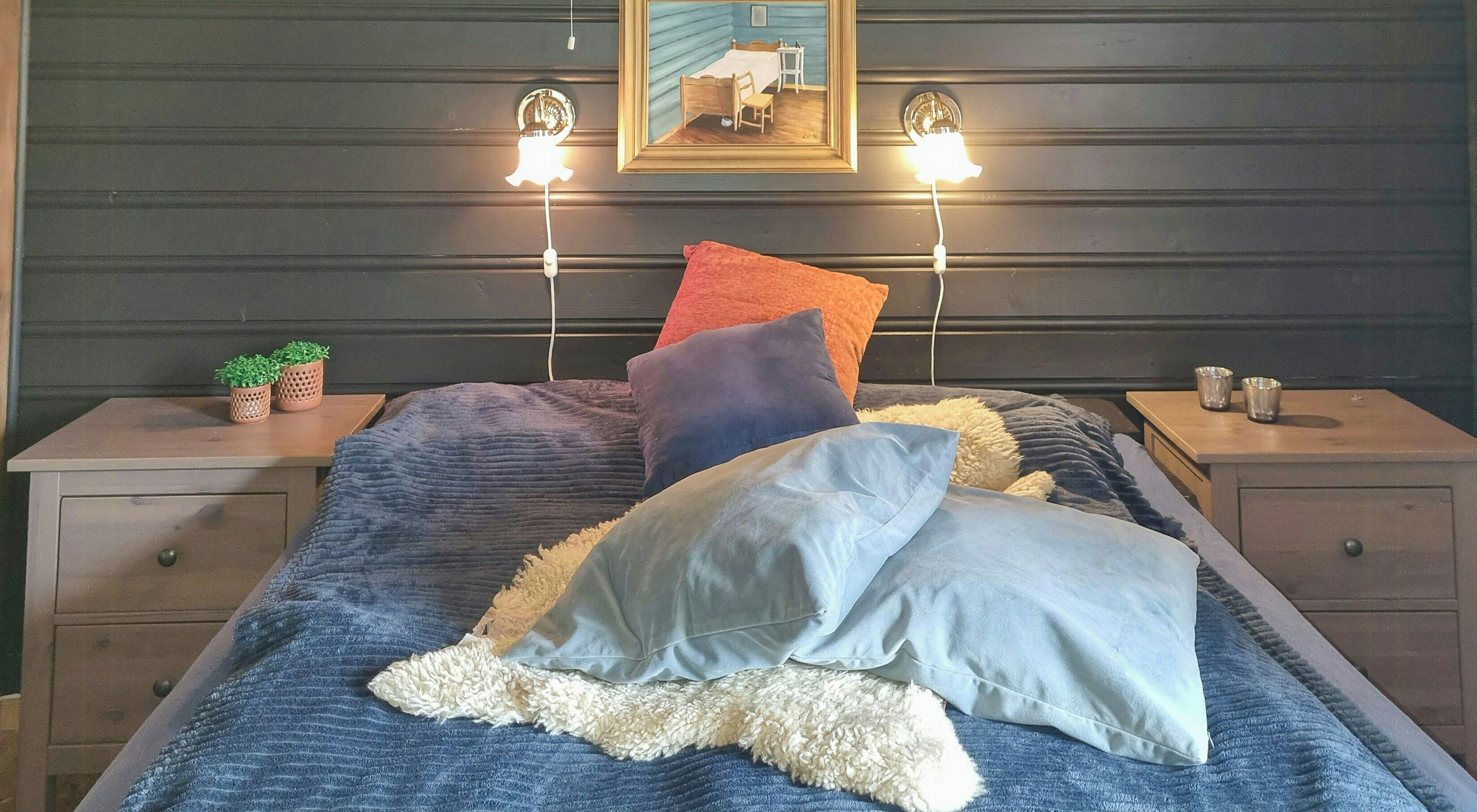 A bedroom with a bed, two bedside tables, a nightstand, a wall-mounted lamp, and a framed picture.