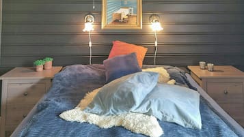A bedroom with a bed, two bedside tables, a nightstand, a wall-mounted lamp, and a framed picture.