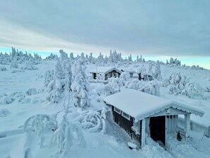 A snow-covered landscape with a wooden cabin and a small shed.