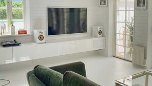 Een moderne woonkamer met een grote flatscreen-tv, witte wanden, een groene bank en een glazen salontafel.