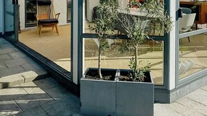 Een modern huis met een glazen patio, een houten stoel en een kleine plantenbak.
