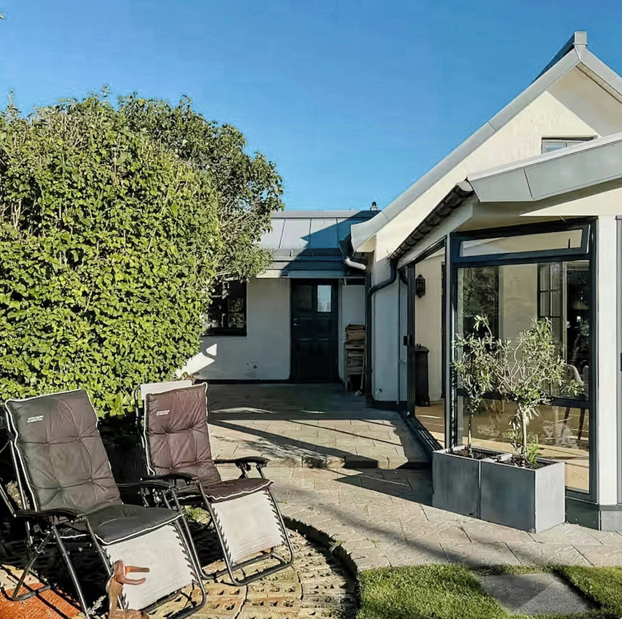 Una casa moderna con patio, mobiliario exterior y un gran árbol.