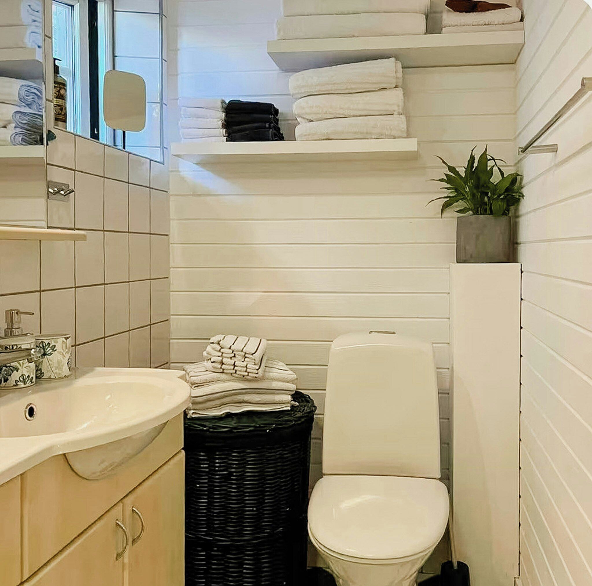 Une petite salle de bain comprenant un lavabo, des toilettes et des serviettes pliées rangées sur une étagère.
