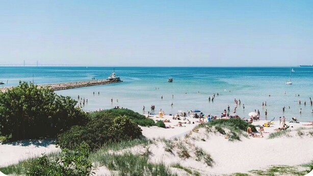 Een strand met mensen, een pier en boten.
