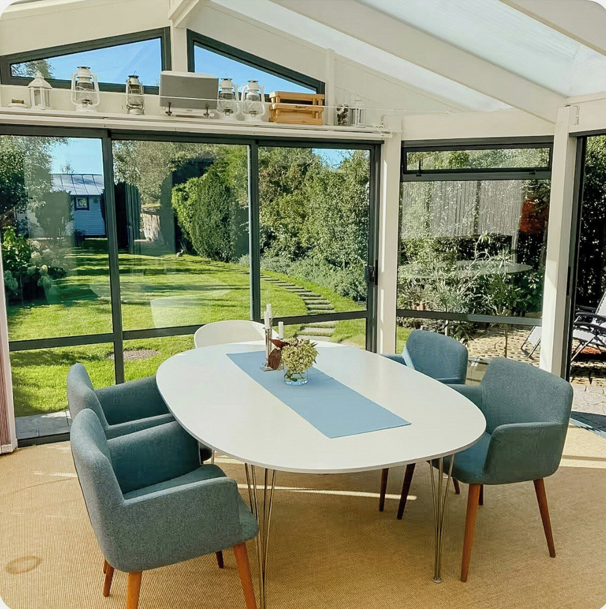Een moderne eetruimte met een ronde tafel en vier stoelen, grote ramen met uitzicht op een verzorgde tuin.