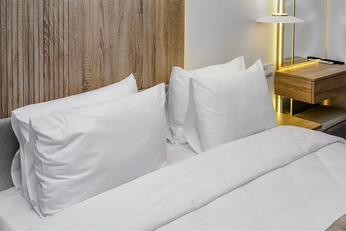 Una habitación de hotel moderna con una pared de acento de madera, una mesita de noche con lámpara y una cama bien hecha.
