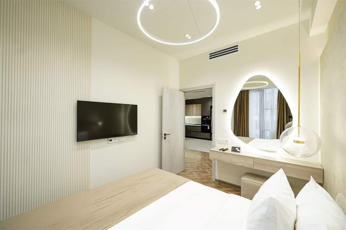 Habitación de hotel con cama, televisor montado en la pared, escritorio con espejo y lámpara moderna.