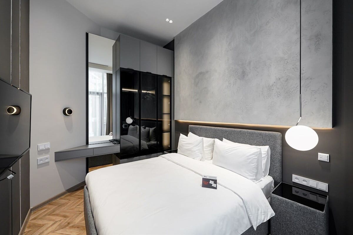 Habitación de hotel moderna con una cama grande, armario empotrado, espejo y mesita de noche.