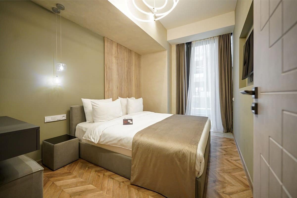Habitación de hotel con cama, mesita de noche y televisor montado en la pared.