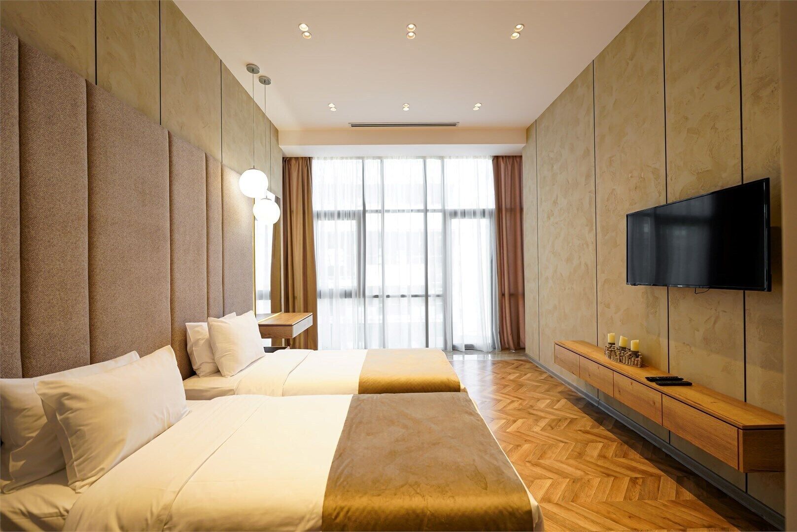 Ein Hotelzimmer mit zwei Betten, einem Fernseher, einer hölzernen Bank und einem großen Fenster.