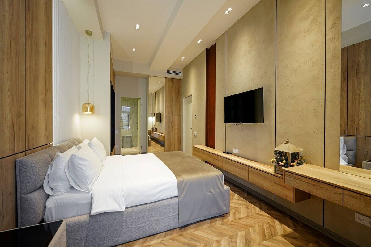 Una habitación de hotel moderna con una cama grande, un televisor montado en la pared y un tocador de madera.