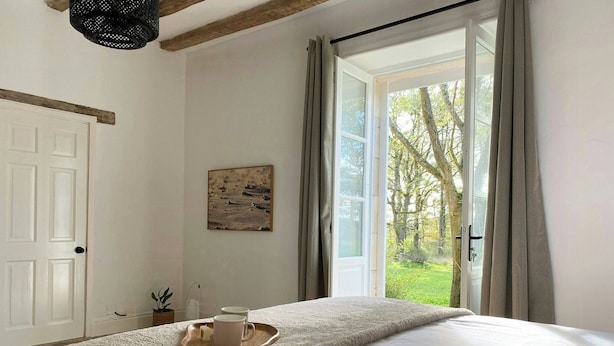 A bedroom with a bed, a window with curtains, a door, and a wall-mounted picture. - Peaceful cottage near Saint-Savin Abbey (Journet)