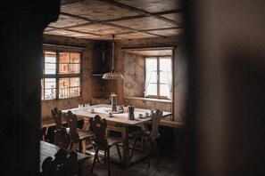 Un comedor rústico con una mesa y sillas de madera, una lámpara colgante y ventanas con cortinas.
