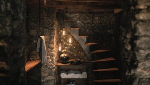 Un interior rústico de piedra con una escalera de madera, una lámpara colgante y un estante con toallas dobladas.