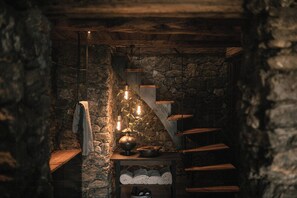 Un interior rústico de piedra con una escalera de madera, una lámpara colgante y un estante con toallas dobladas.