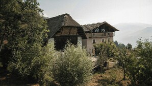 Un edificio rústico con techo de paja y un balcón, rodeado de follaje y montañas al fondo.
