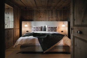 Un dormitorio con paneles de madera, una cama, dos lámparas de noche y almohadones estampados.